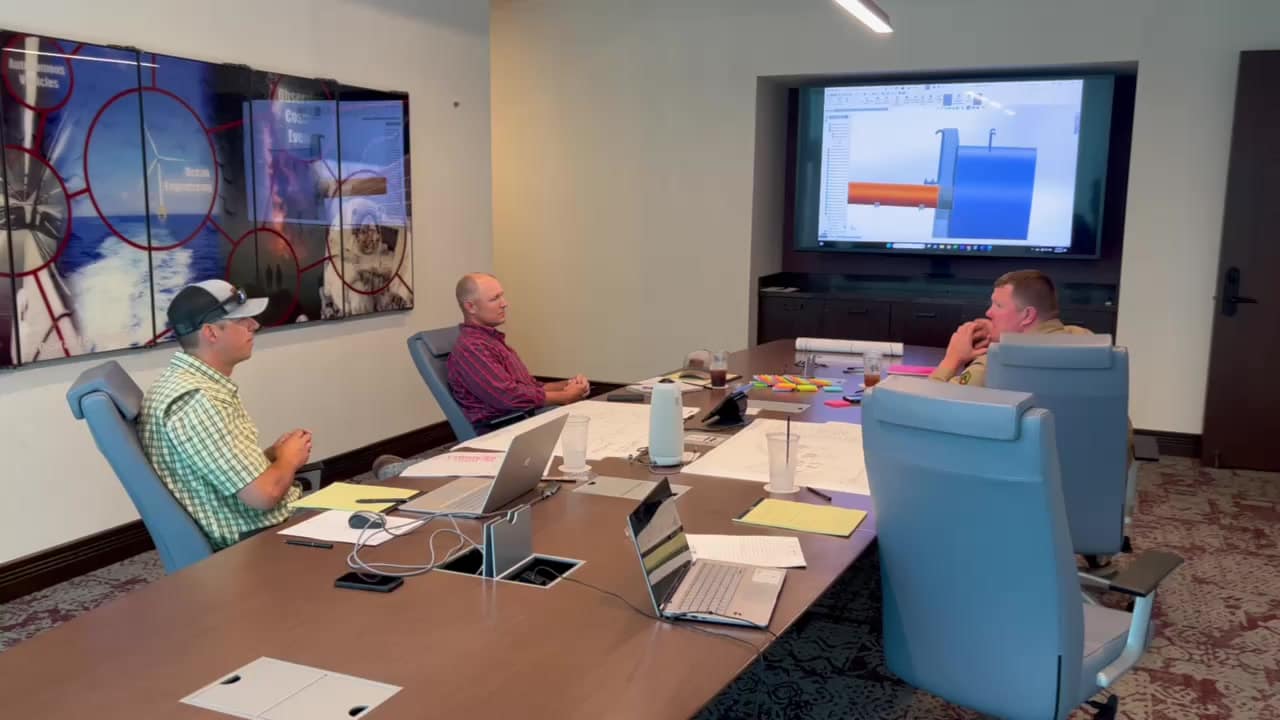 3 men in a conference room viewing a diagram on a tv