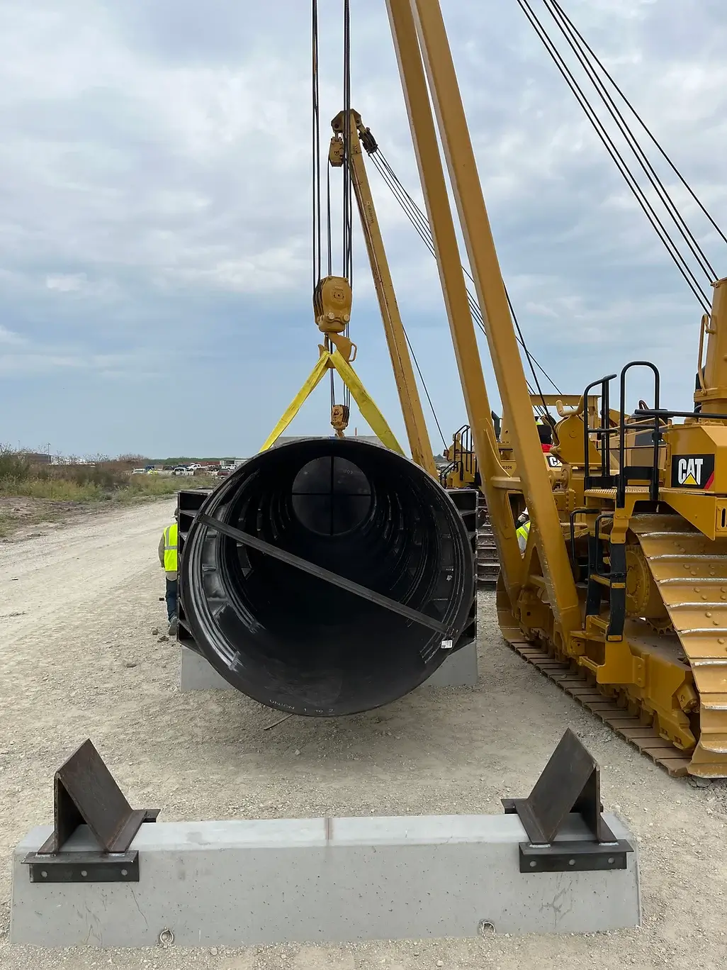 a side view of a large metal pipe suspended by many cranes